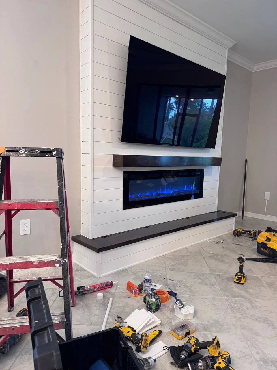 Installation stage of a custom shiplap fireplace media wall in Houston with TV, electric fireplace, wood mantel, tools, and finish carpentry work.
