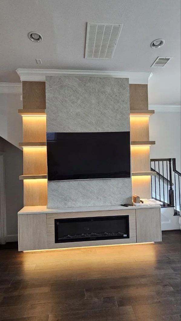 C-Series media wall in Houston featuring a wall-mounted TV, linear electric fireplace, illuminated display niches, and crown molding integration.