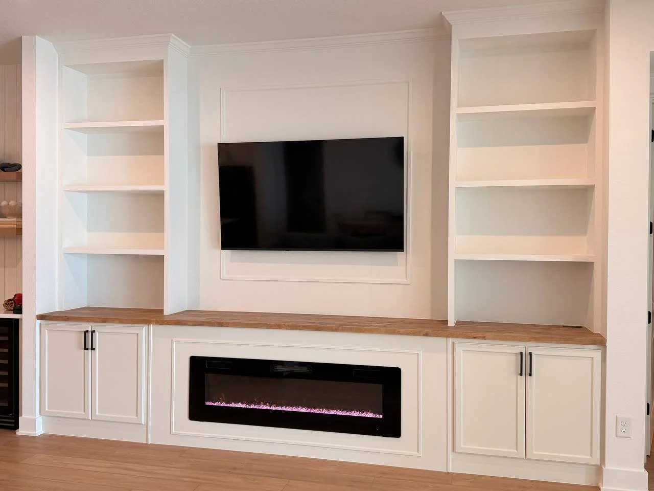 Custom built-in entertainment center in Tampa with white cabinets, open shelves, stained wood countertop, mounted TV, and linear electric fireplace