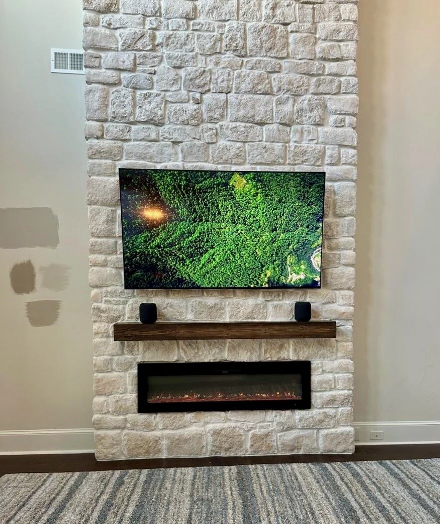 close view of stone fireplace media wall with floating wood mantel, TV installation and linear electric fireplace