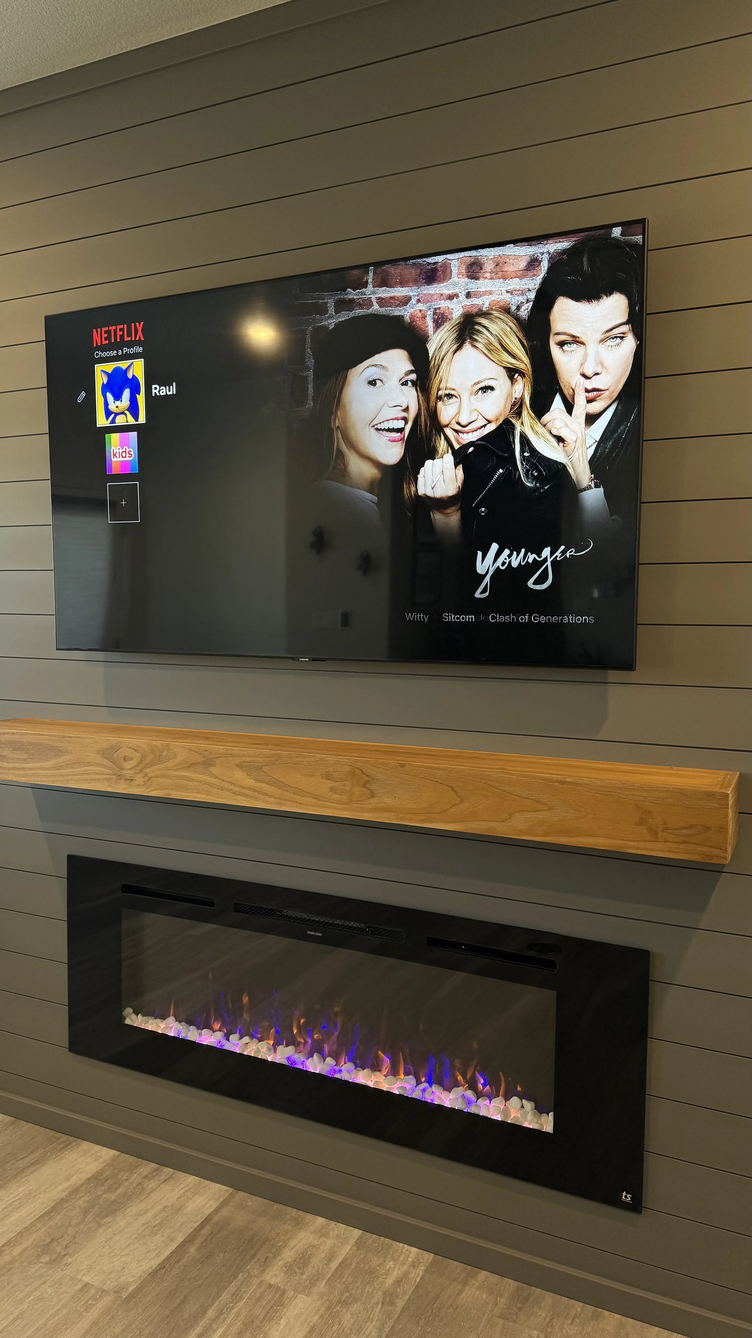 linear electric fireplace installed in dark shiplap fireplace media wall with mounted TV