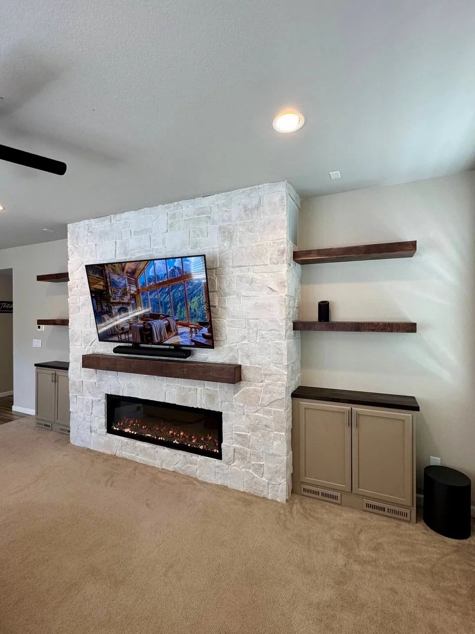 Light stone fireplace media wall in Castle Rock featuring taupe storage cabinets, dark wood countertops, matching floating shelves, and a linear electric fireplace.