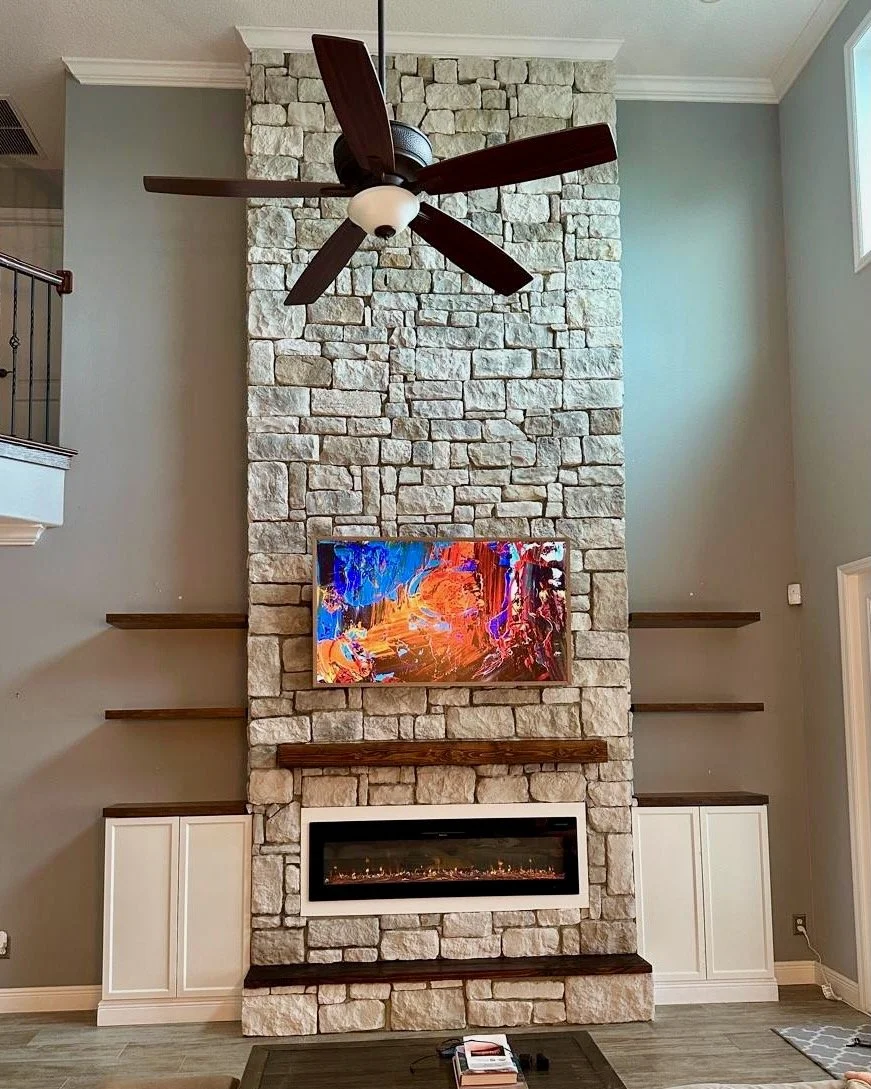 Stone fireplace media wall with TV and floating shelves in Melbourne, FL – front view.