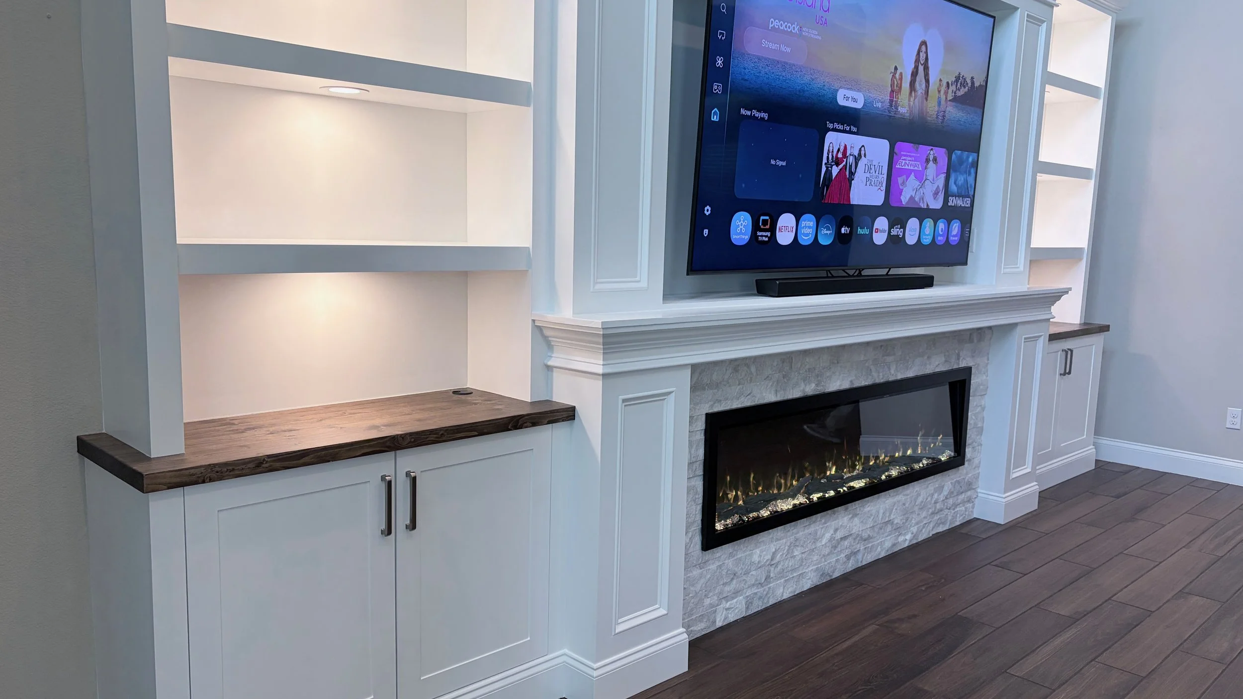 Custom built-in entertainment center detail showing cabinet storage, wood countertop, fireplace surround and illuminated shelving