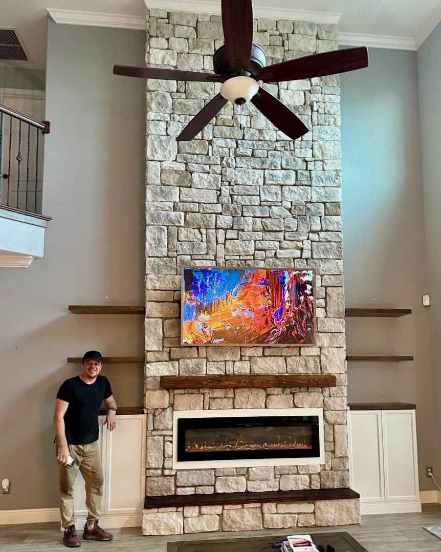 Side angle of modern stone media wall with cabinets and floating wood shelves.