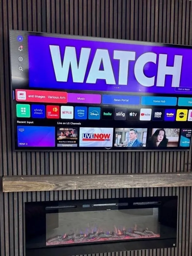 Smart TV displaying a menu with categories like images, music, and different streaming apps, mounted above an electric fireplace.