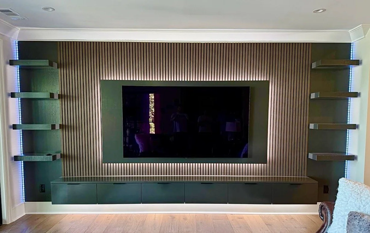 Modern custom TV media wall in Charlotte with vertical wood slats, dark floating cabinet and illuminated display shelves