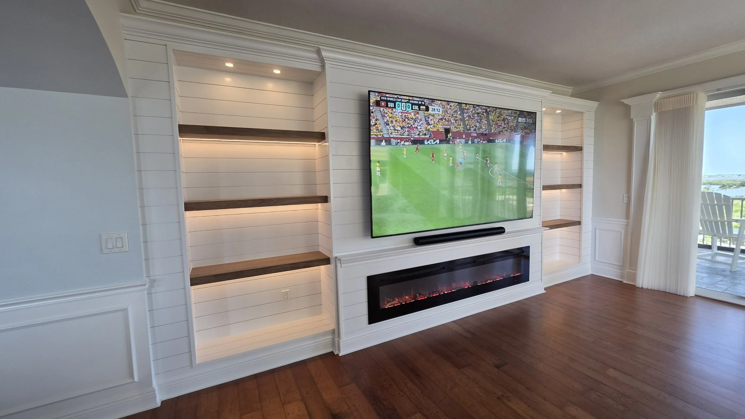 Custom media wall with illuminated built-in shelves, decorative trim, crown molding and electric fireplace in Cape Coral Florida
