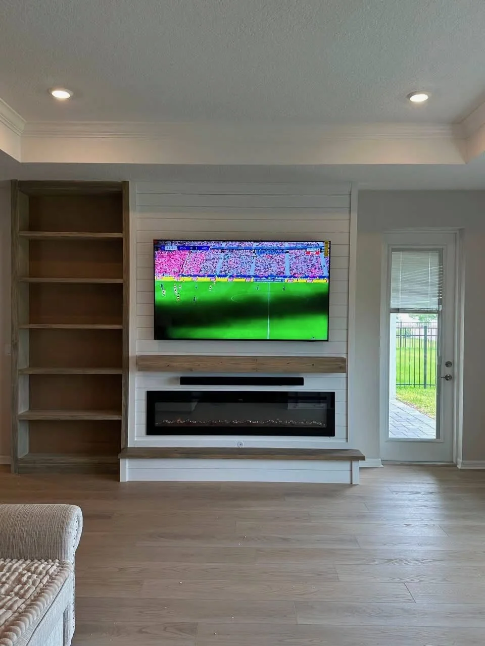 Front elevation of a custom media wall with open shelving, electric fireplace, and wall-mounted television