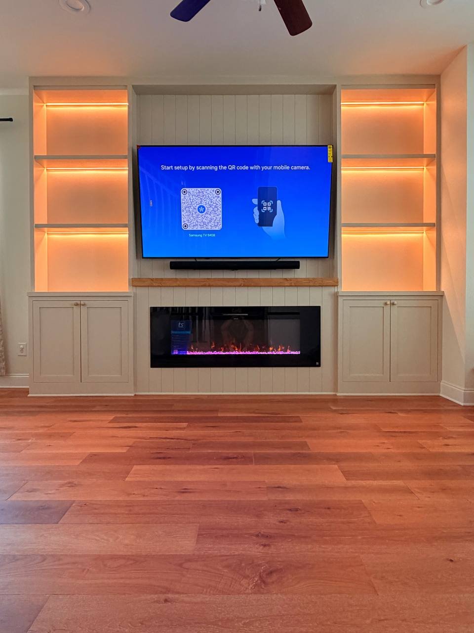 Shiplap-style fireplace wall with built-in storage cabinets, illuminated shelving, mounted TV, and linear fireplace in Orlando.