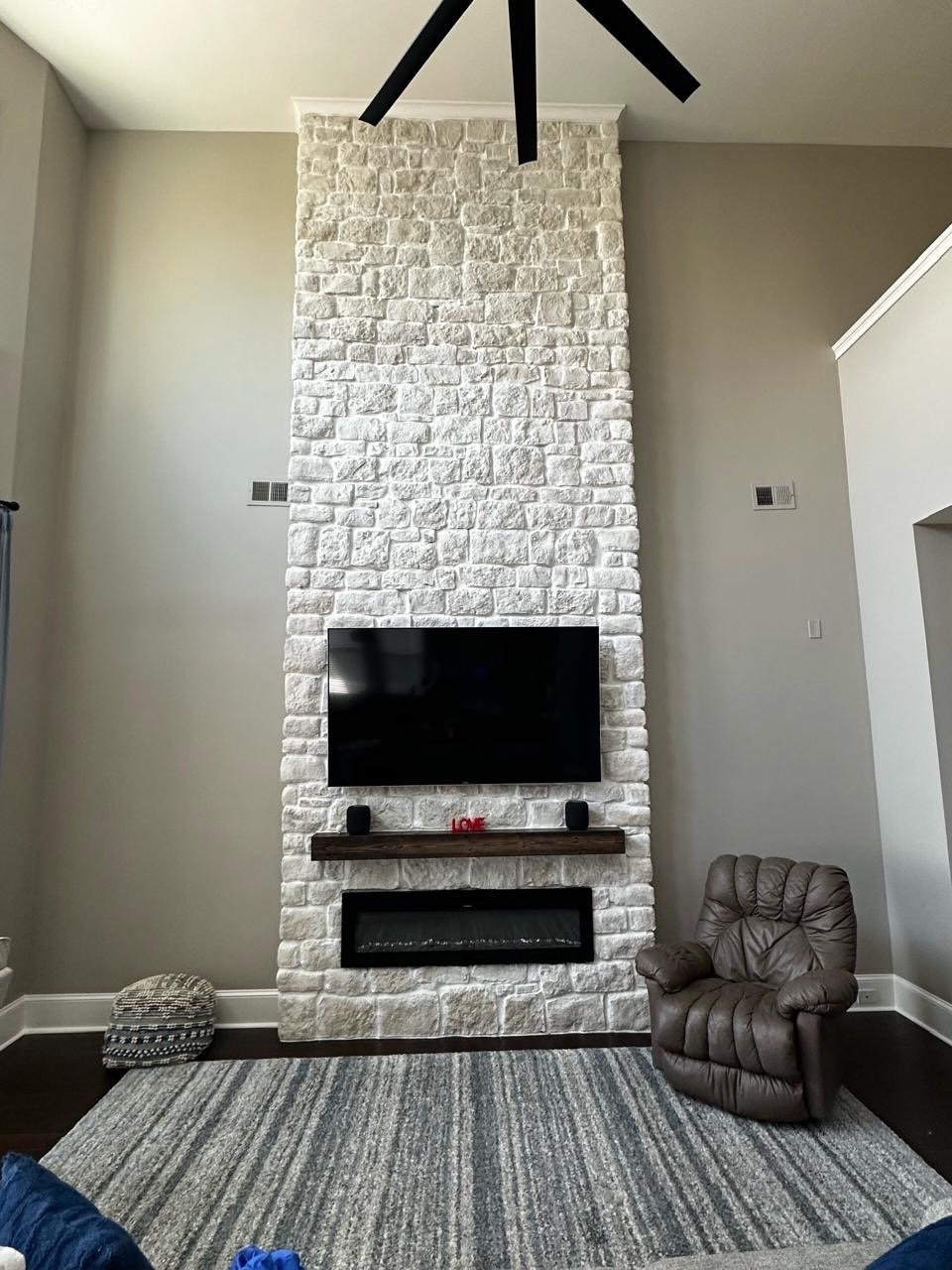 stone fireplace media wall with mounted TV and electric fireplace in high ceiling Orlando living room