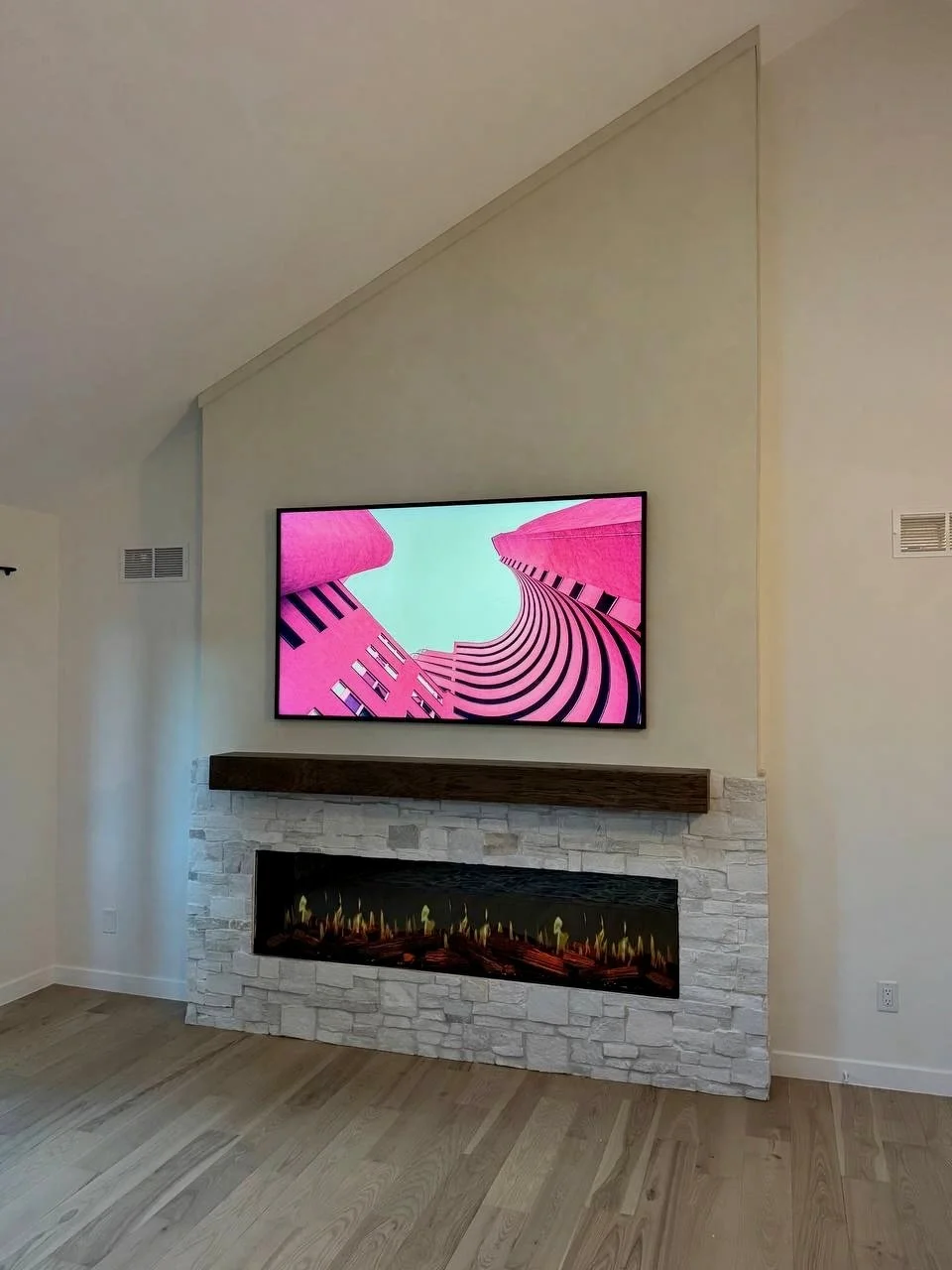 Custom fireplace media wall following a sloped ceiling, with limewash above the wood mantel and light stone surrounding the fireplace.