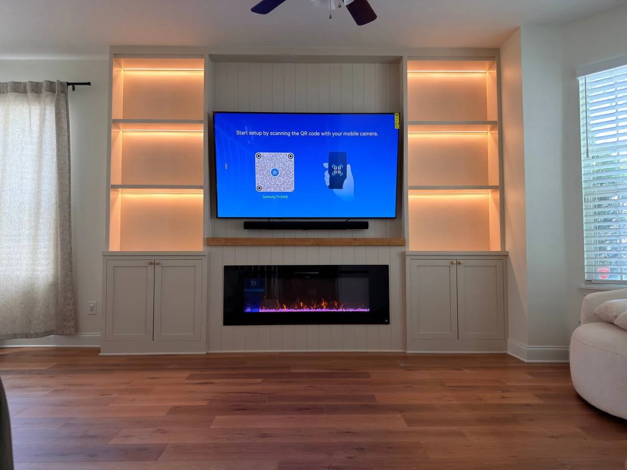 Custom fireplace media wall in Orlando with built-in cabinets, illuminated shelves, mounted TV, wood mantel, and linear electric fireplace.