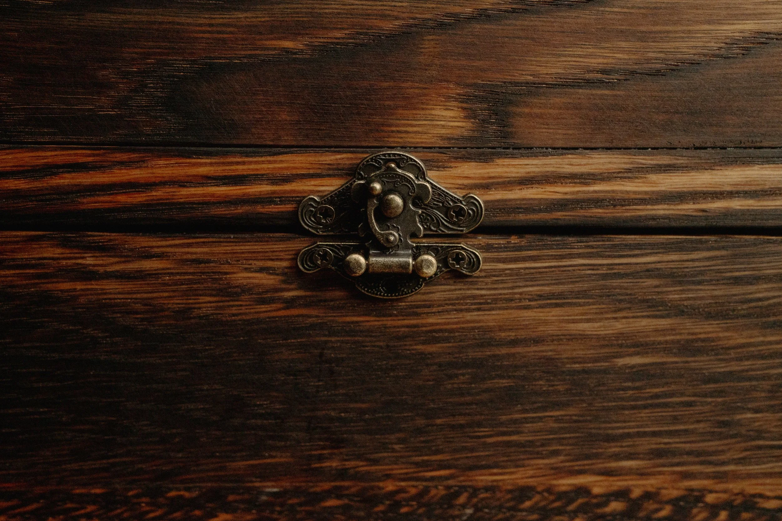 Close-up of an ornate vintage latch on a dark wood surface.