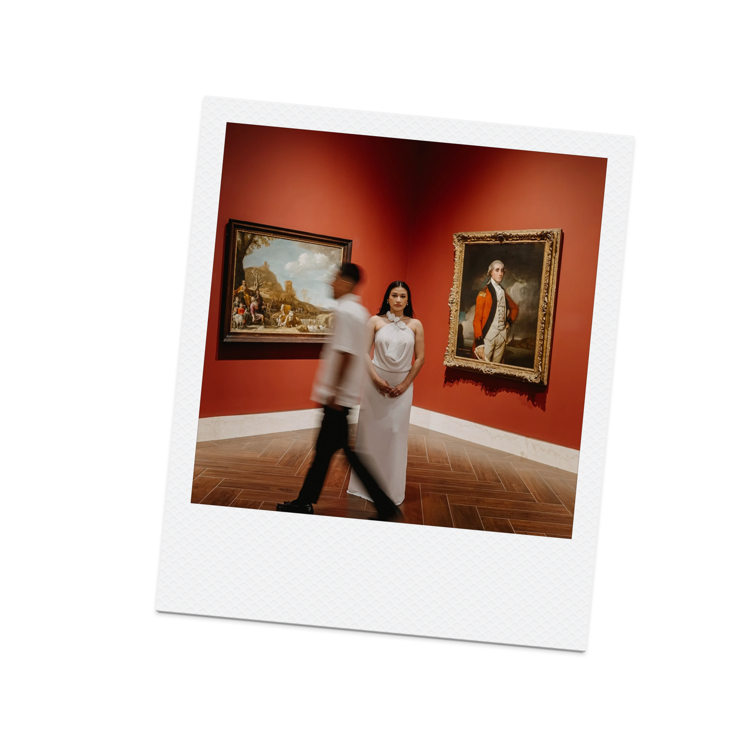 Two people at an art gallery, a woman in a white dress standing still and a man walking past her, with paintings on a red wall behind them.