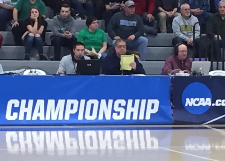 People sitting behind a table with a blue banner that reads 'Championship' and an NCAA logo, inside a gymnasium during a sporting event.