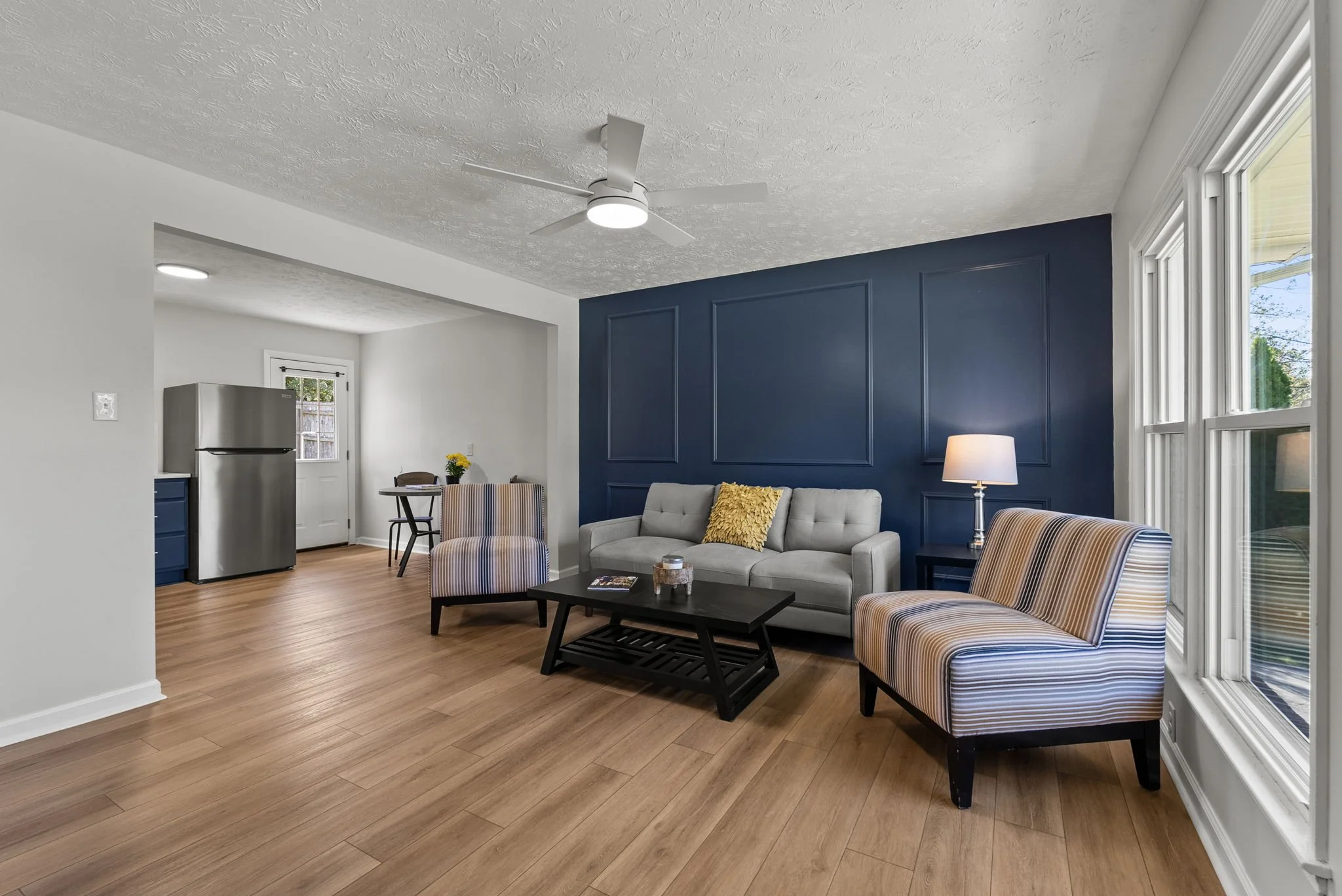 A bathroom vanity with two sinks, black faucets, and two large arched mirrors above. The vanity has a wooden cabinet with black handles. There are black light fixtures with round bulbs mounted above each mirror and a black towel ring on the wall.