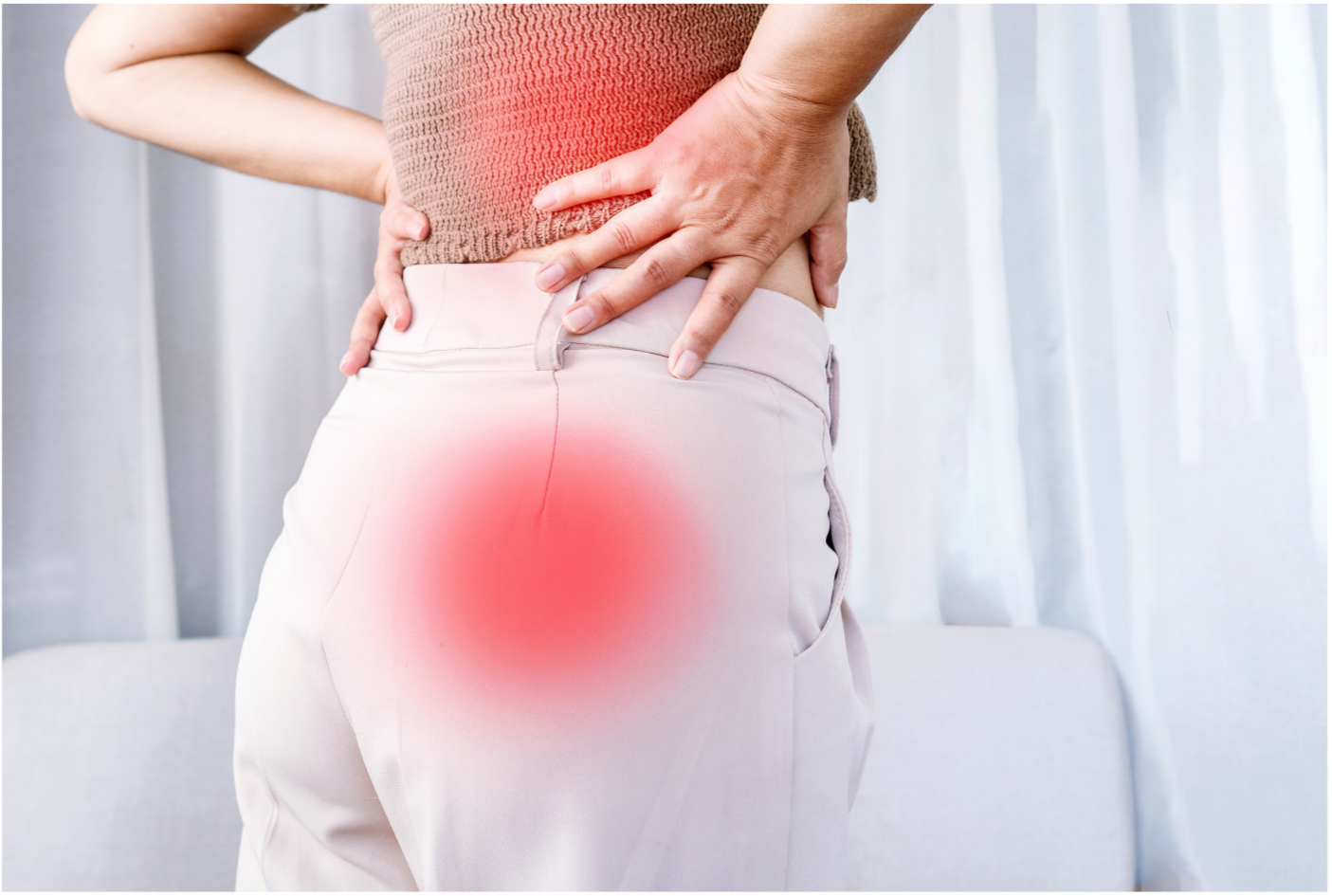 A female patient wearing white pants and a tan shirt is facing away from the camera, holding her lower back with both hands. Her lower back as well as her gluteal muscles are highlighted red, indicating pain. A text box says "Sciatica"