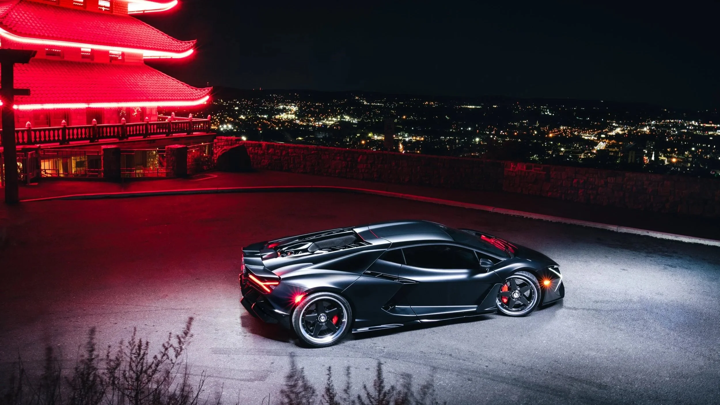 A red Honda NSX parked on the side of a paved road with green bushes and trees in the background.