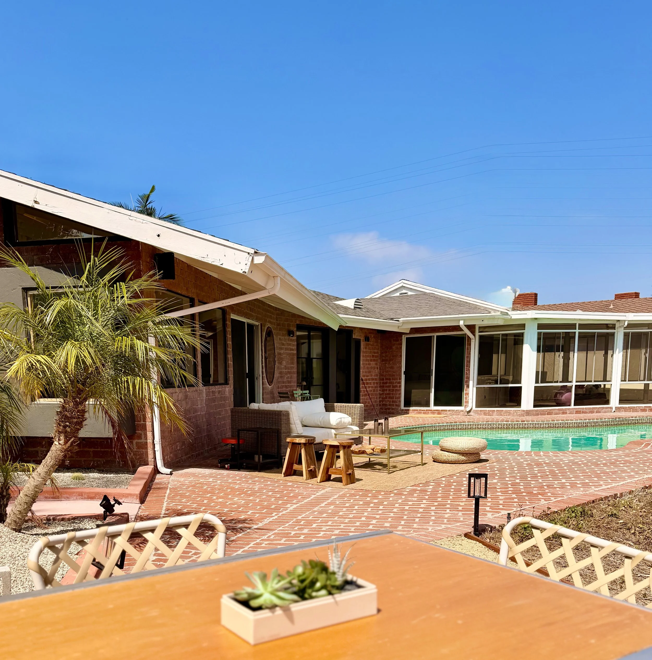 Backyard patio with brick paving, outdoor furniture, a swimming pool, and a house with large windows and a screened porch.