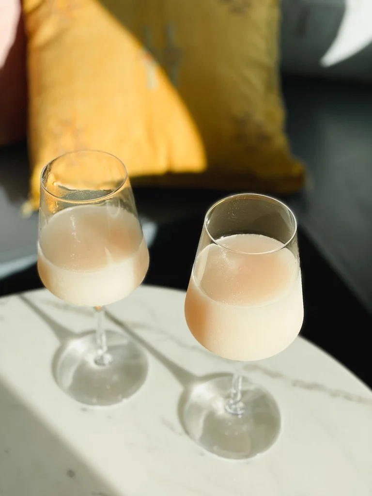 Two glasses of champagne on a white surface with a yellow pillow and dark sofa in the background