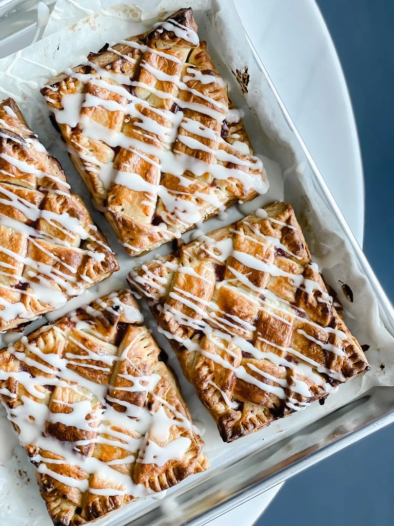 Four pieces of apple pie with a drizzle of white icing on top, arranged in a tray lined with parchment paper.
