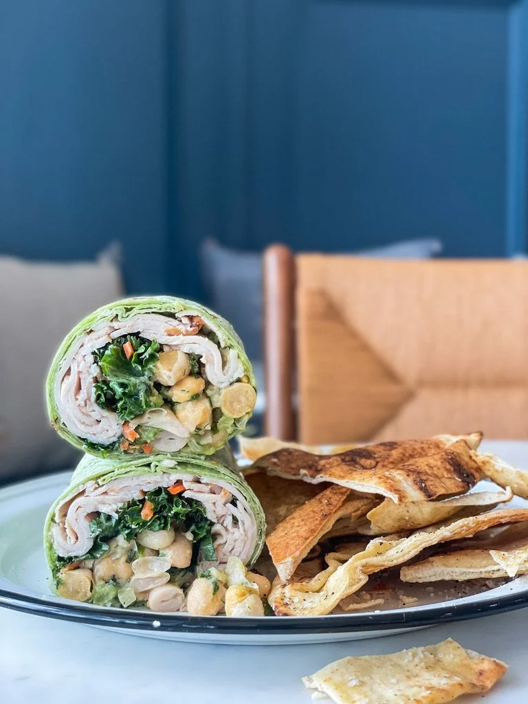 Two chicken wrap halves filled with lettuce, chickpeas, and vegetables, served with flatbread chips on a white plate.