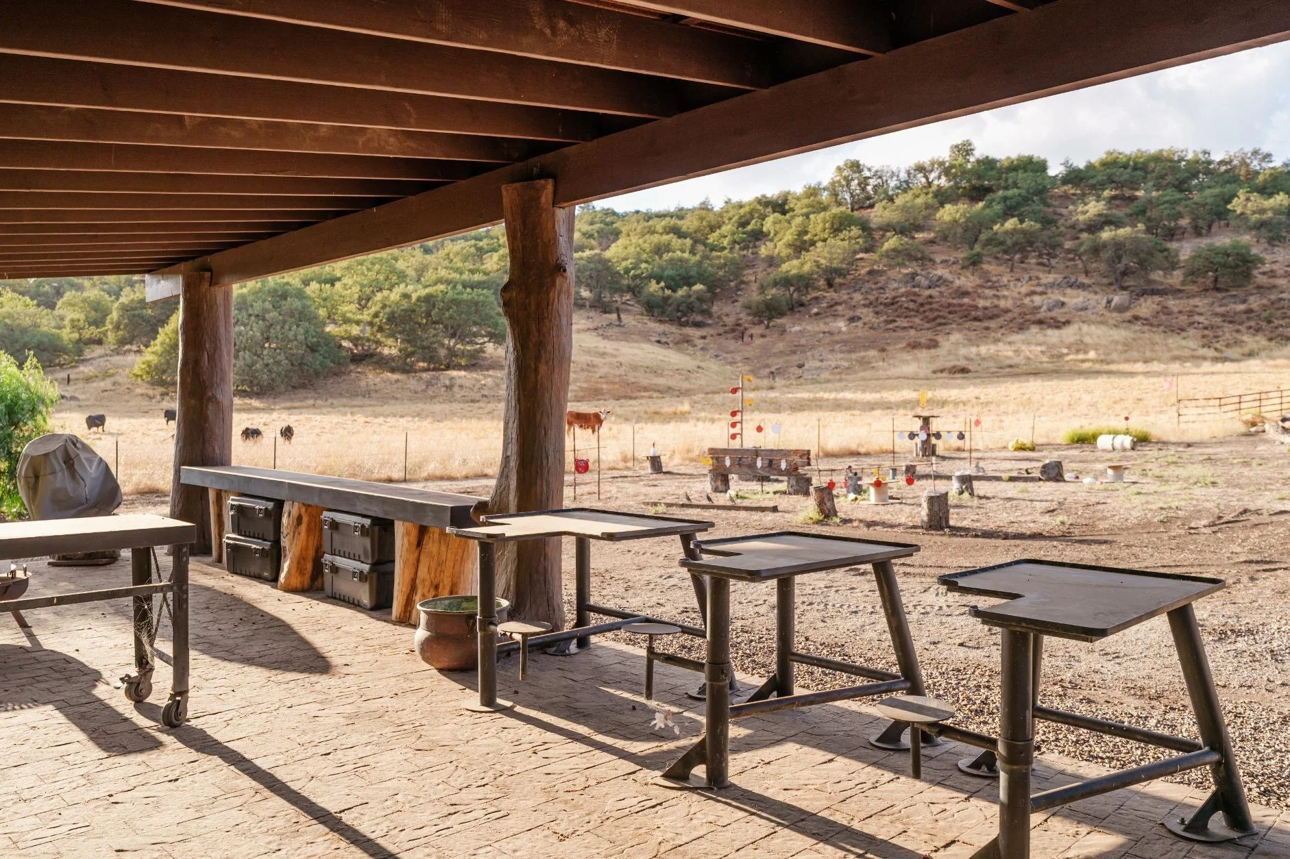 Outdoor patio with tables and a view of a rural field with cows and hills in the background.