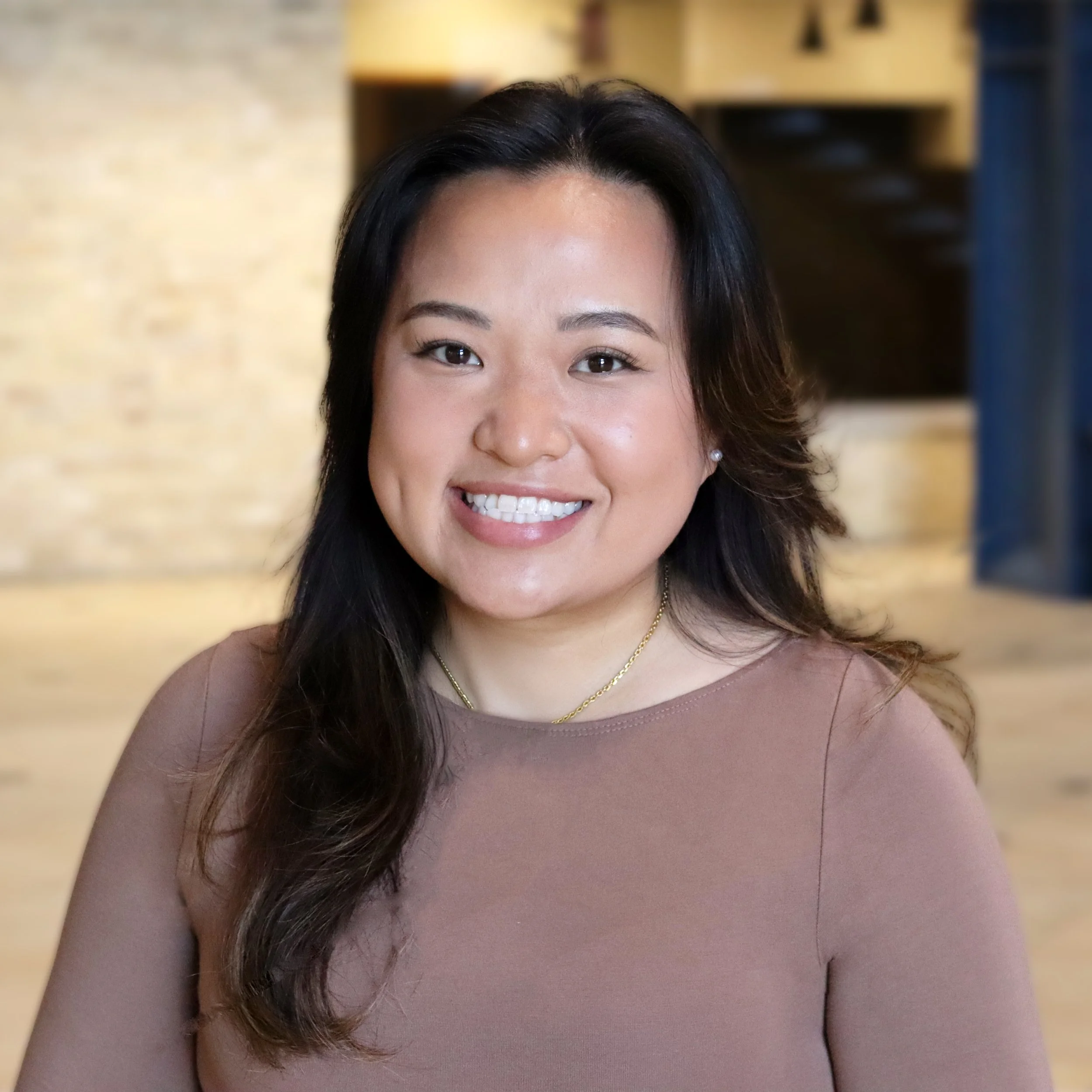 A woman with long, wavy hair, smiling, in an indoor setting.