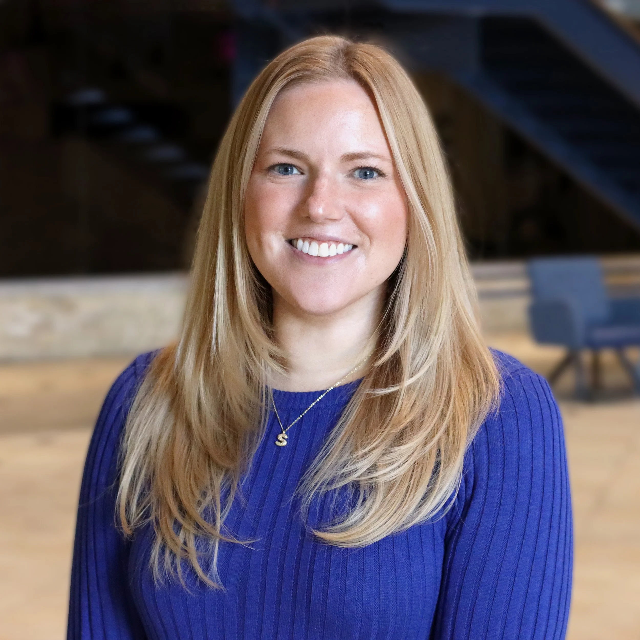 Portrait of a young woman with long blonde hair, wearing a red dress with lace details on the sleeves, smiling indoors.