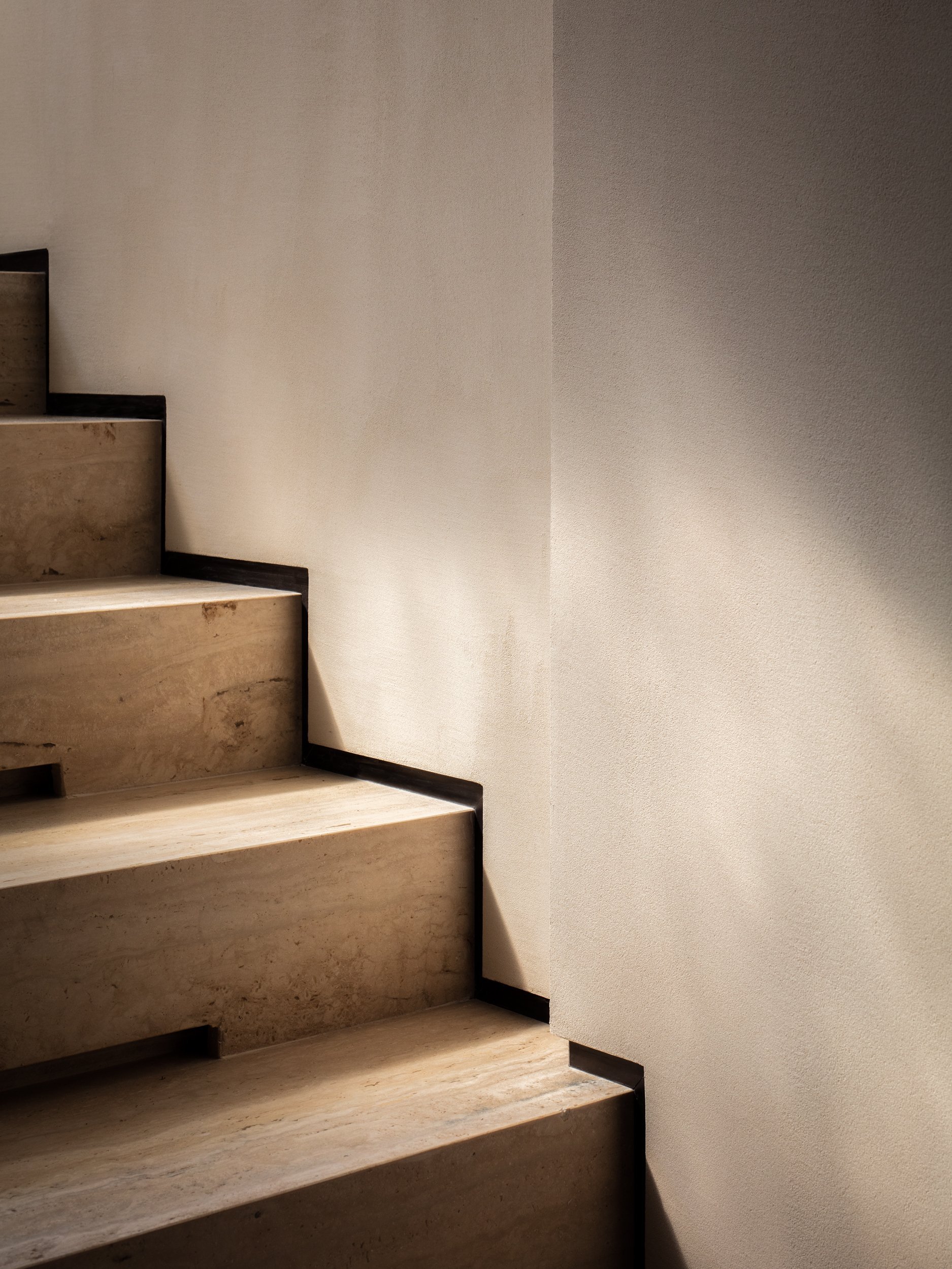 Close-up of a beige marble staircase with black trim along the edge, next to a plain light-colored wall.