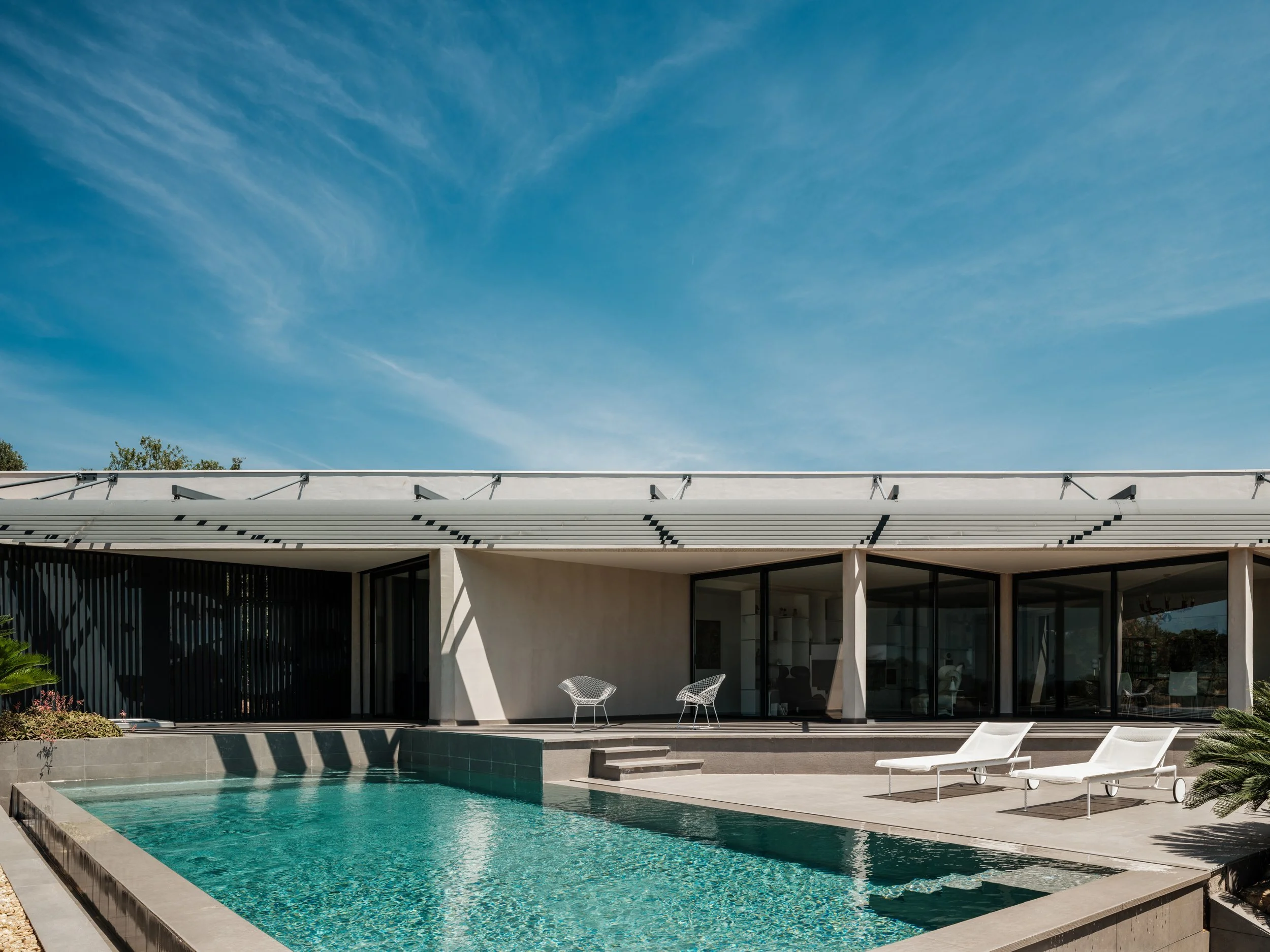 Modern house with a swimming pool, lounge chairs, and outdoor seating under a blue sky.