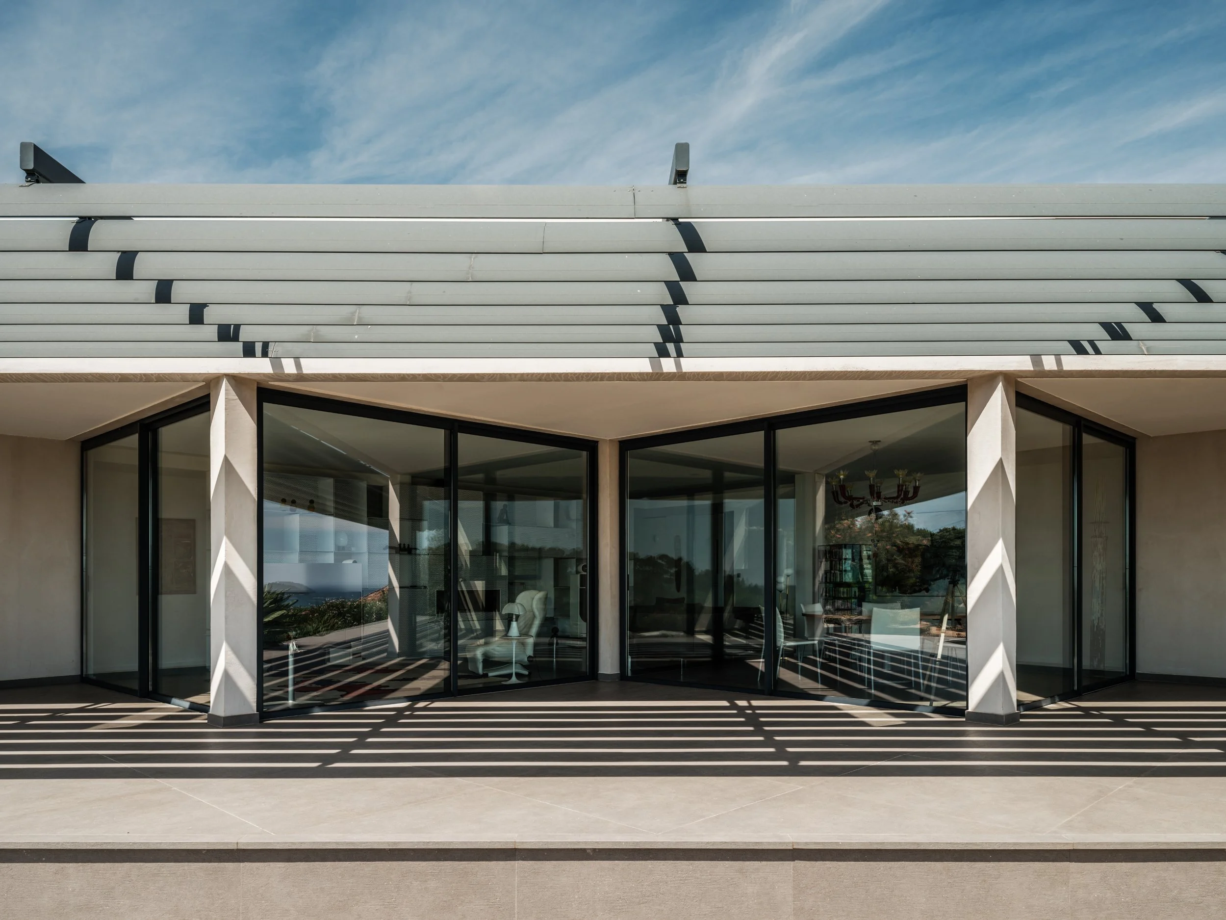 Modern house with large glass sliding doors, a shaded balcony, and a blue sky with scattered clouds.