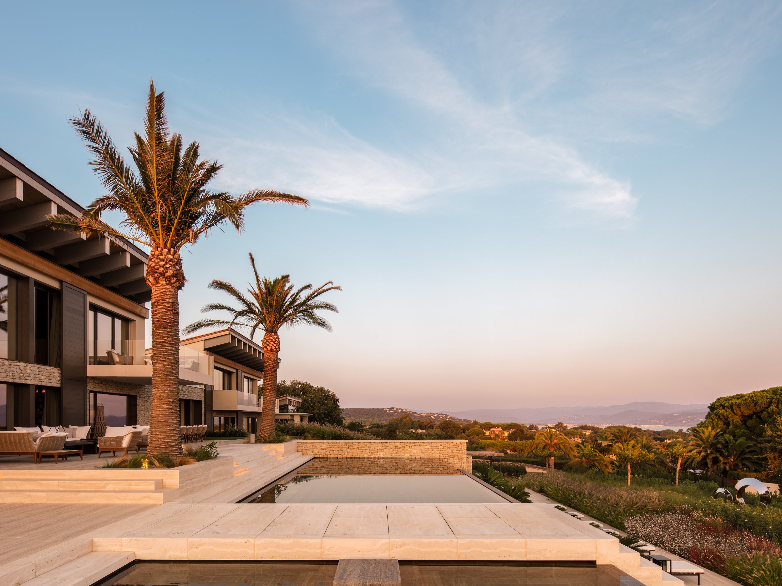 Luxury modern house with palm trees, swimming pool, and scenic landscape at sunset