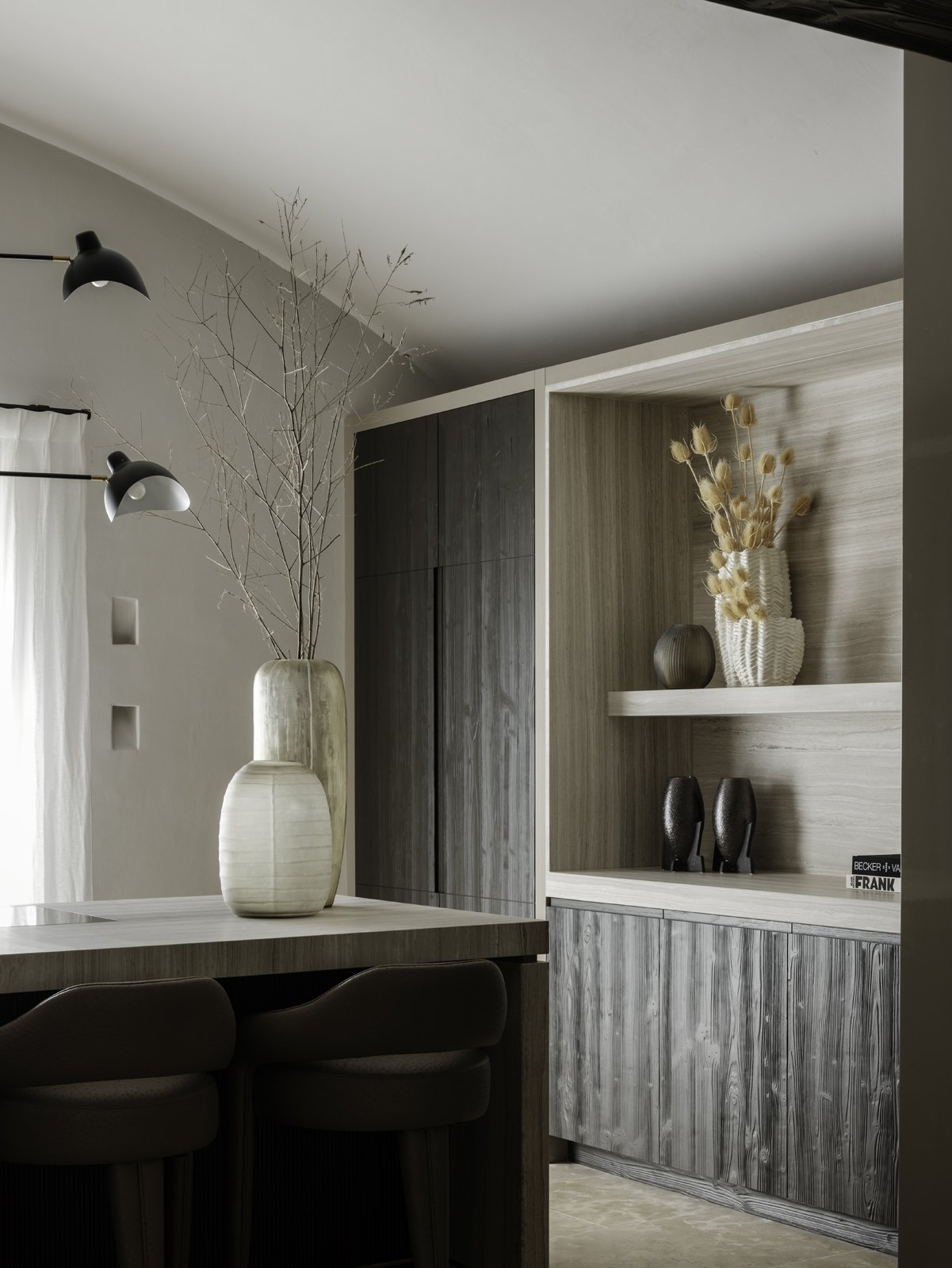 Modern dining area with a large beige vase holding bare branches on a wooden table, a built-in wooden cabinet with dark and light wood finishes, and decorative vases on shelves, illuminated by black wall-mounted lamps and sheer curtains near a window