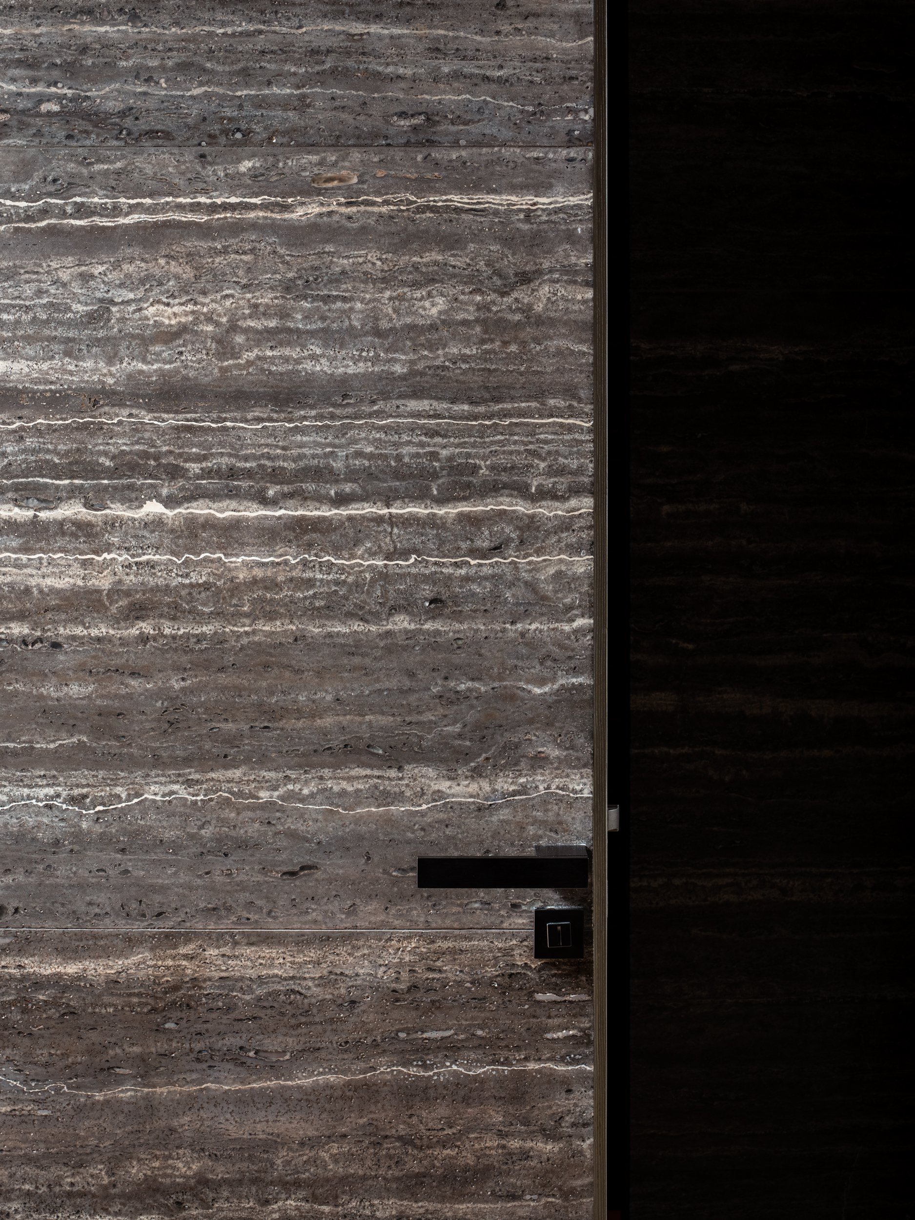 Close-up of a modern bathroom wall with brown and gray textured marble tiles, black door handle, and black trim.