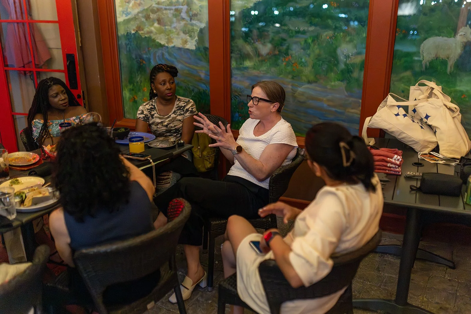 A small group sits around a restaurant table in conversation, with one person gesturing while others listen.