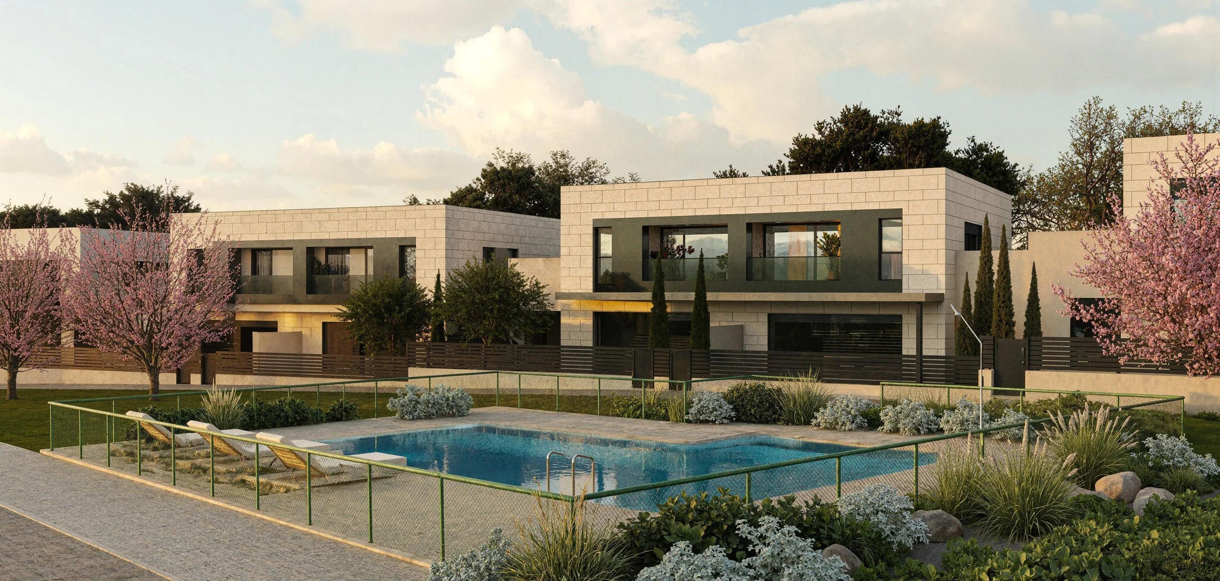 Modern residential complex with two-story houses, landscaped gardens, pink flowering trees, a swimming pool, and a cloudy sky.