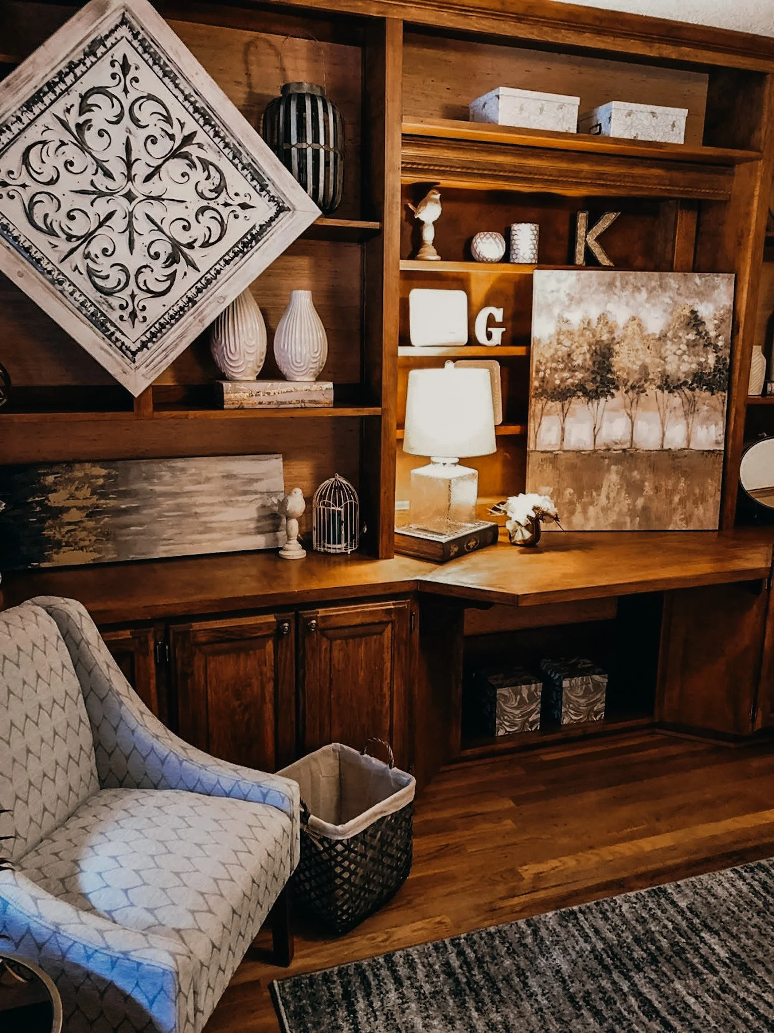 A wooden wall with decorative shelves holding vases, lanterns, and framed art, next to a seating area with a patterned chair, a basket, a lamp, and a striped rug.