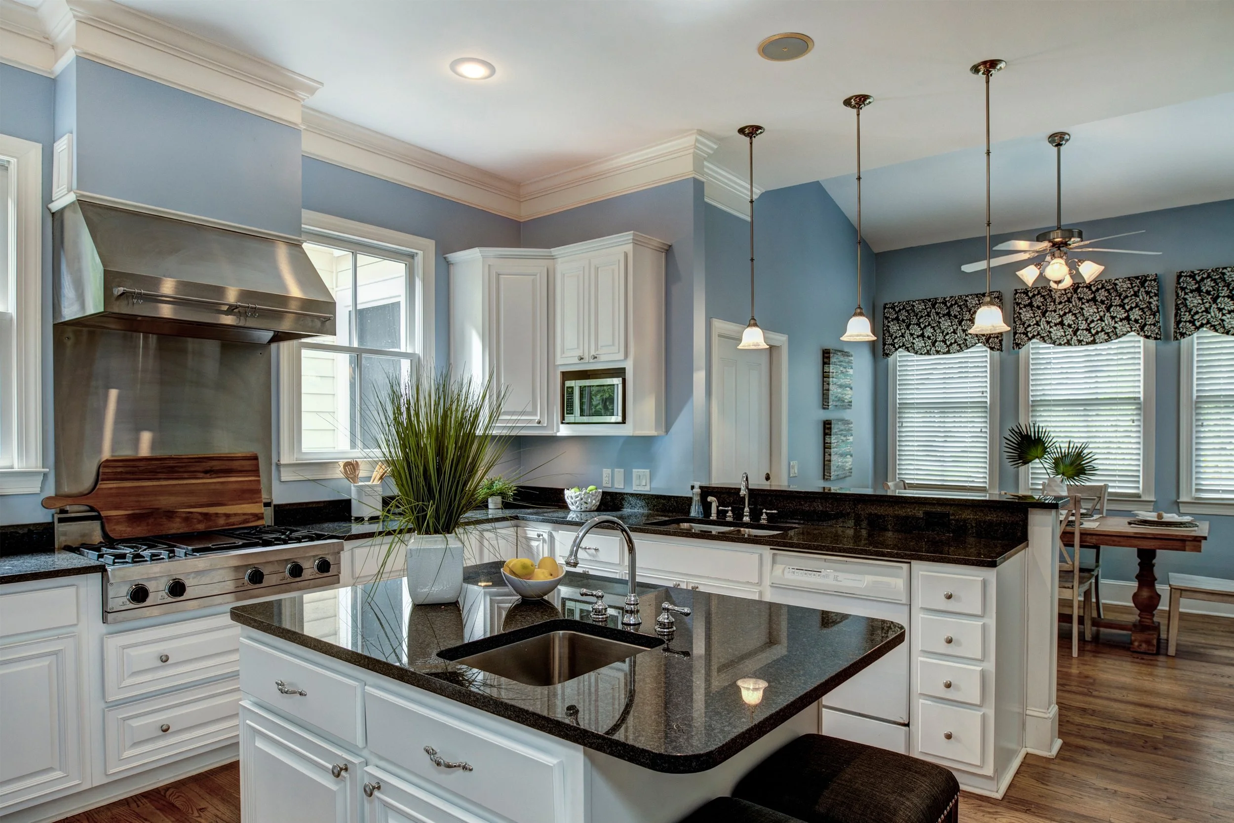 Modern kitchen with white cabinets, black granite countertops, stainless steel appliances, a kitchen island, and a dining area with windows and blinds.