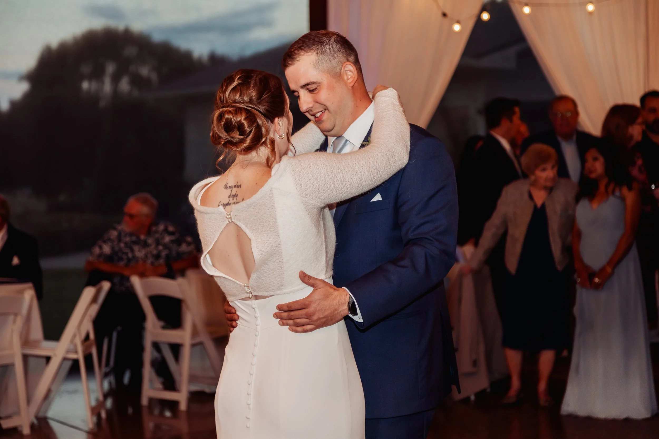 A bride and groom dance closely together in a wedding reception, with guests watching in the background.