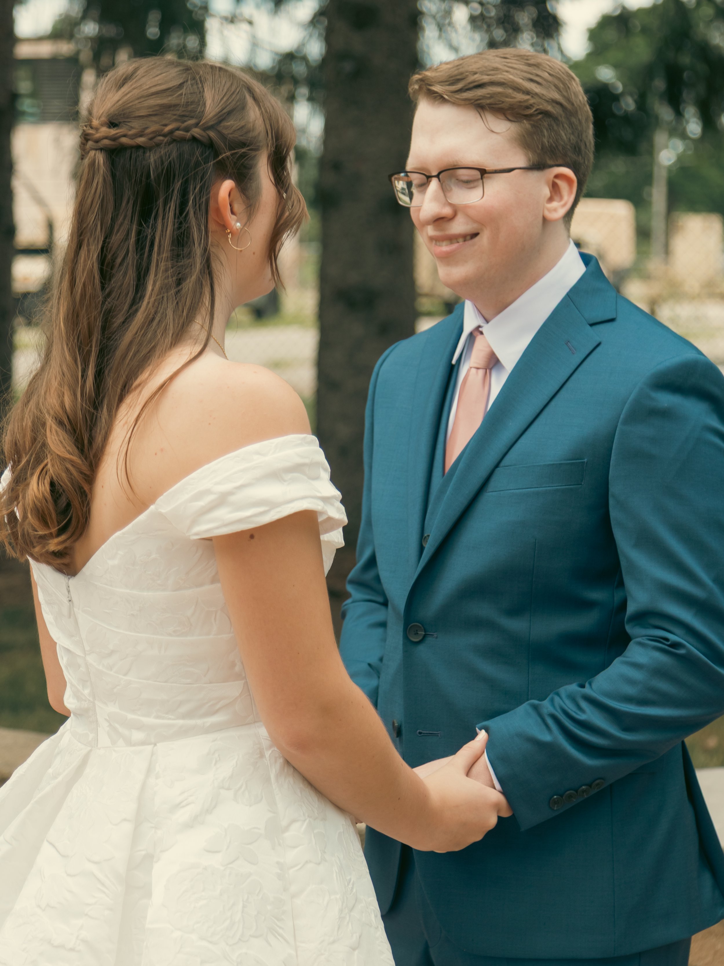 A bride and groom holding hands outdoors during their wedding ceremony, smiling at each other.