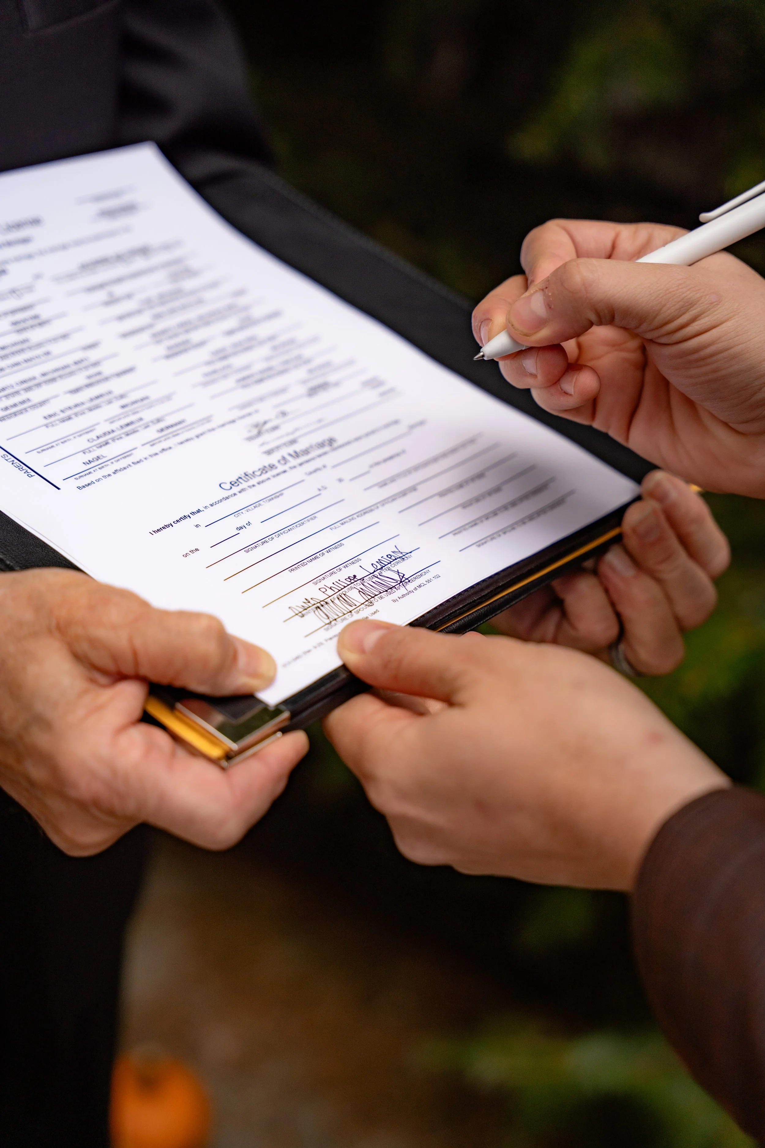 A person holding a clipboard with a certificate of marriage, signing it with a white pen.