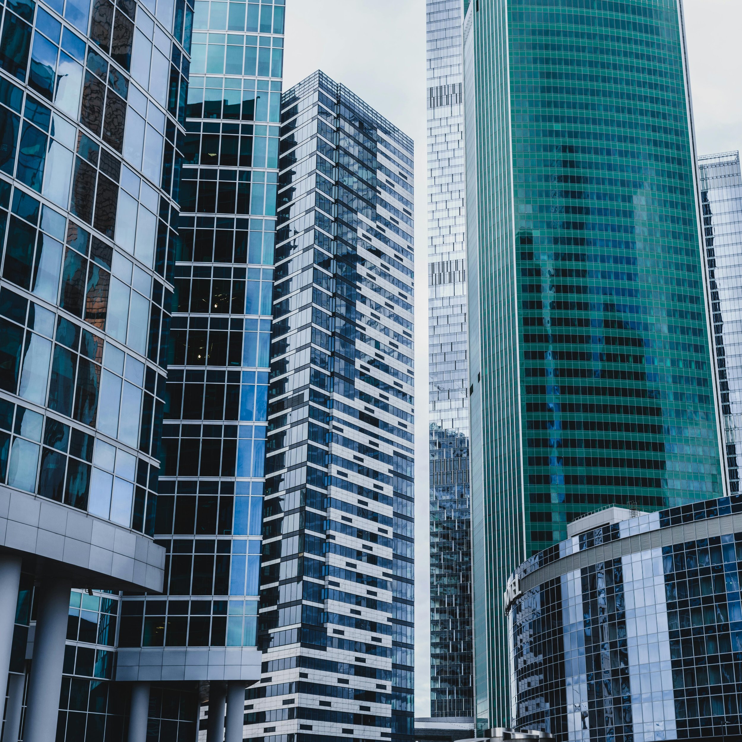 A group of modern glass skyscrapers in a city, reflecting the sky and surrounding buildings.
