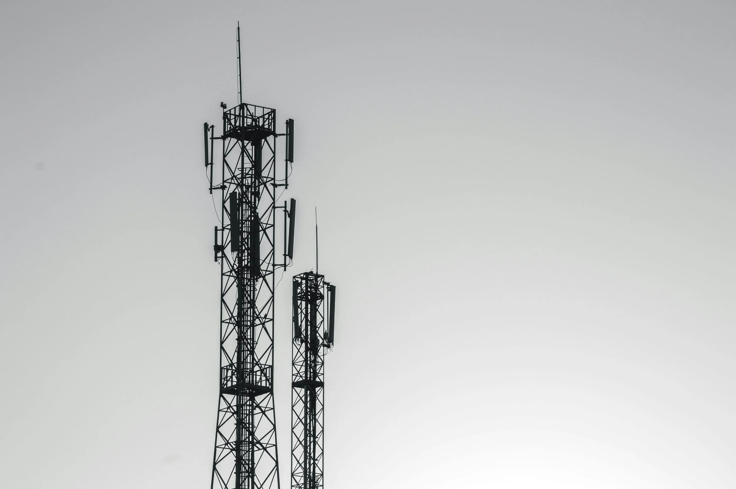 A communication tower with multiple antennas against a cloudy sky.