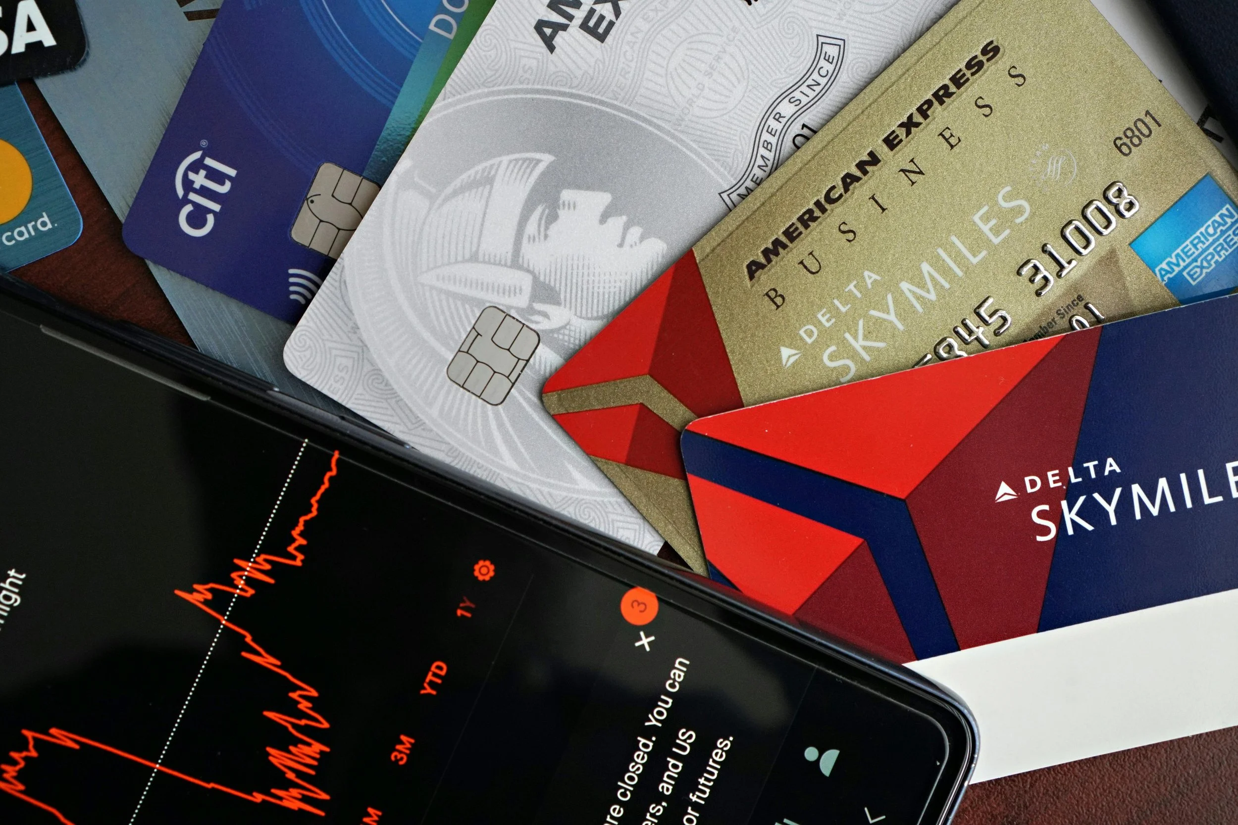 Close-up of several credit cards, including American Express and Delta SkyMiles, on top of a smartphone displaying a red line graph.