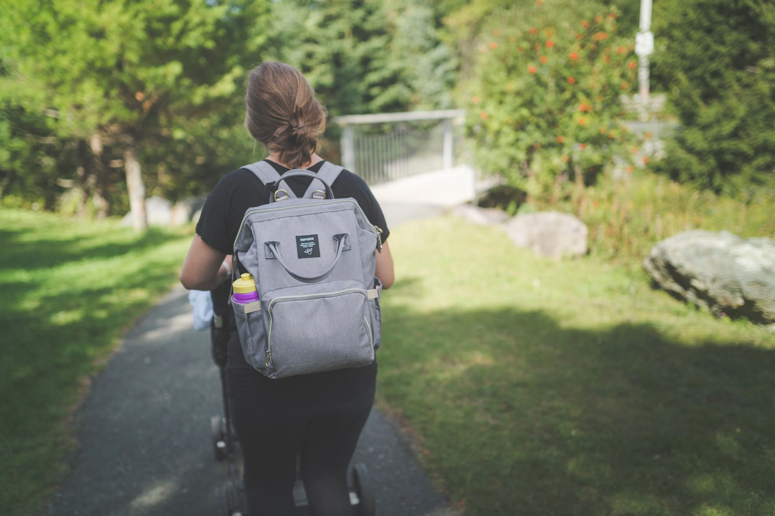 woman carrying diaper bag, pushing stroller in park