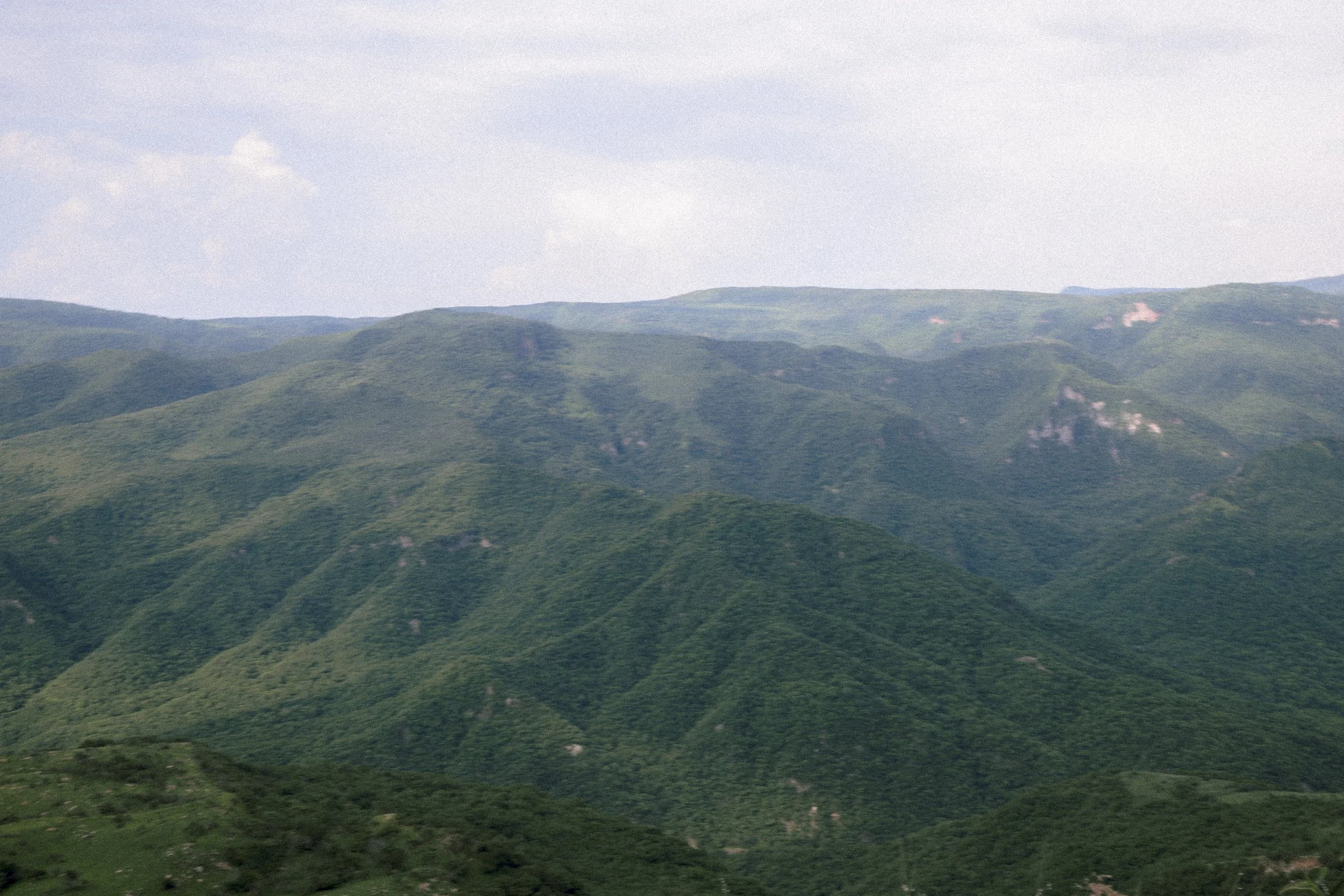 Vista panorámica de montañas cubiertas de vegetación verde bajo cielo parcialmente nublado.