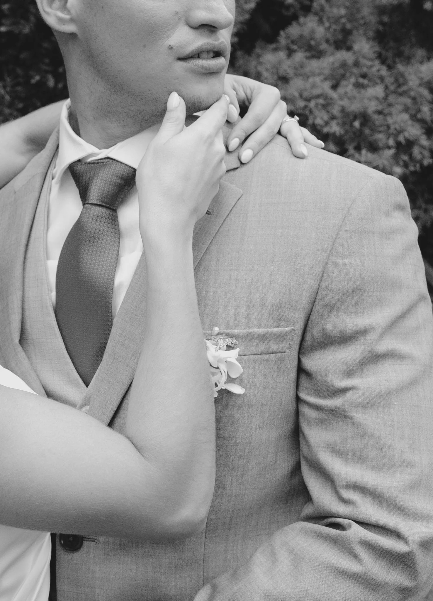 Una pareja en un abrazo romántico, con enfoque en la parte superior del cuerpo, en un entorno al aire libre, en blanco y negro.