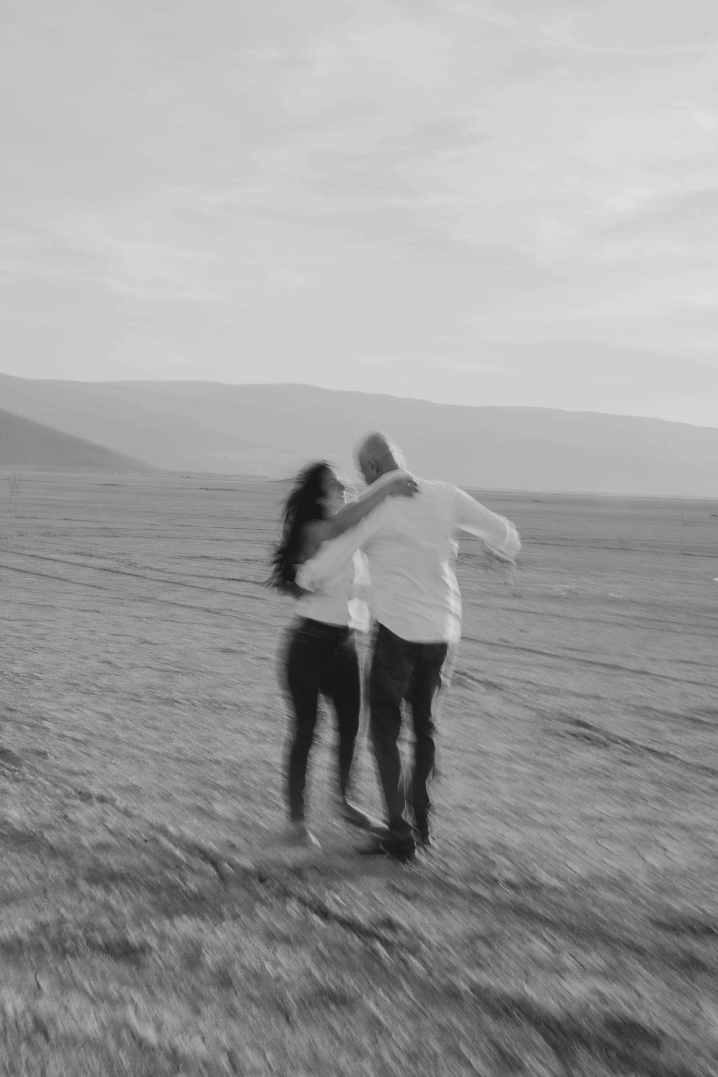 Una pareja bailando en un campo abierto con montañas al fondo, en blanco y negro.